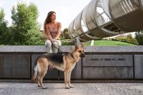 Vue de face du gai propriétaire féminin penché avec chien berger allemand à la frontière sur le remblai — Photo de stock