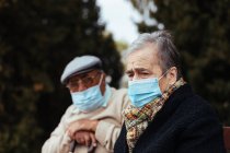 Vue latérale d'un couple âgé portant un masque facial dans la rue alors qu'ils regardent ailleurs un après-midi d'hiver — Photo de stock
