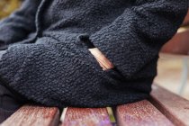 Вид сбоку на анонимную пожилую женщину, залезающую в карман пальто, сидя на скамейке в деревянном парке — стоковое фото