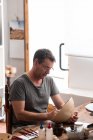 Чоловік сидить за столом з пензлями та малює ескізи на керамічній пластині ручної роботи — стокове фото