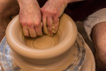 Crop unrecognizable sculptor with equipment giving shape while sculpting with brown clay on throwing wheel — Stock Photo