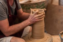Cultivar escultor irreconhecível com equipamento dando forma ao esculpir com argila marrom na roda de lançamento — Fotografia de Stock