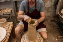 Cultivo escultor irreconocible con equipo que da forma mientras esculpe con arcilla marrón en la rueda de lanzamiento - foto de stock