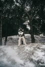 Собака породы хаски стоит на сугробах в мегаполисе с высунутым языком, глядя в камеру в зимний день под ясным небом на природе рядом с холмом, покрытым деревьями — стоковое фото