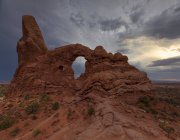 Amazing landscape with arched formation in red rock near rare vegetation located in national park against cloudy sky in USA — Stock Photo