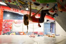 Vue latérale de l'athlète féminine forte dans le mur d'escalade de vêtements de sport dans le centre de bloc moderne — Photo de stock