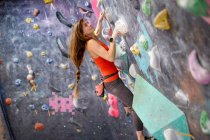 Вид сбоку на сильную спортсменку в спортивной одежде, карабкающуюся стену в современном боулдеринговом центре — стоковое фото