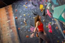 Vista lateral de la fuerte atleta femenina en la pared de trepado de ropa deportiva en el centro de bouldering moderno - foto de stock