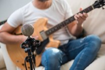Vintage microphone near crop unrecognizable bearded male musician playing acoustic guitar on sofa — Stock Photo