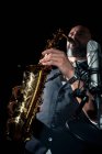 Desde abajo cultivo de músico masculino en traje con clase de pie cerca de micrófono y tocando saxofón alto durante concierto de jazz - foto de stock