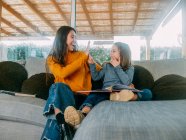 Cheerful female teenager and sibling having fun while spending time on cozy sofa and looking at each other at home — Stock Photo