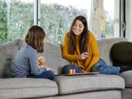 Content female teen with unrecognizable sister playing game on soft couch while spending time in house — Stock Photo