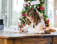 Обрізати маленьку дівчинку, малюючи різнокольоровими олівцями на аркуші паперу у світлій кімнаті — стокове фото