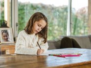 Рисунок маленькой девочки с разноцветными карандашами на бумажном листе в светлом помещении — стоковое фото