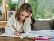 Рисунок маленькой девочки с разноцветными карандашами на бумажном листе в светлом помещении — стоковое фото