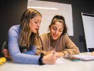 Student with marker explaining information for smiling classmate while working on homework assignment together against whiteboard — Stock Photo