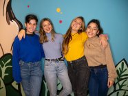 Щасливі молоді жінки посміхаються яскраво, стоячи разом проти барвистої пофарбованої стіни і дивлячись на камеру — стокове фото