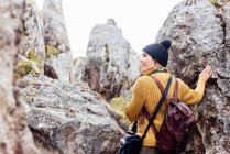 Back view content female traveler wearing warm clothes and hat standing amidst rough rocks and looking away in pleasant thoughts — Stock Photo