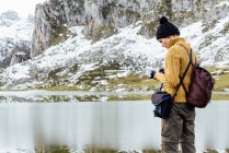 Visão lateral focou jovem fotógrafa em suéter quente tirando fotos na câmera fotográfica profissional de majestosas montanhas ásperas no planalto gramado no dia de outono claro — Fotografia de Stock