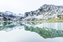 Amazing scenery of rough severe mountain range with slopes in snow and cold frozen lake on bottom on clear winter day — Stock Photo