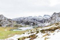 Вражаючий вигляд скелястого снігового гірського хребта біля спокійного озера і простора трав 