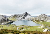 Spettacolare vista della catena montuosa rocciosa innevata vicino al tranquillo lago e spaziosa valle erbosa in una natura tranquilla nelle Asturie — Foto stock