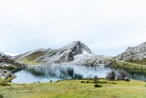 Спектакльный вид на скалистый заснеженный горный хребет рядом с спокойным озером и просторными виллами в спокойной природе Астурии — стоковое фото
