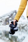 Crop anonymous female tourist in knitwear with professional photo camera against snowy mountain and lake in Asturias — Stock Photo