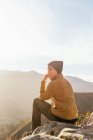 Seitenansicht des Wanderers, der auf Stein sitzt und an sonnigen Tagen die atemberaubende Landschaft des Hochlandtals beobachtet — Stockfoto