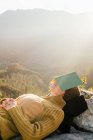 Вид збоку мирної жінки мандрівник лежить на каменях і вкриває обличчя книгою під час сну в горах в сонячний день — стокове фото