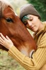Боковой вид нежной женщины, гладящей морду каштанового коня, пасущегося на лугу во время выходных в сельской местности — стоковое фото