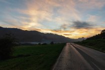 Асфальтована дорога на тлі гірського хребта під світанковим небом ввечері — стокове фото