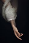 Из выше урожая тонкая женская рука в влажно-белом полупрозрачном рукаве, плавающем в темной воде озера — стоковое фото