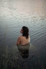 Обратный вид на неузнаваемую женщину-путешественницу в ткани, отражающейся в чистой озерной воде против деревьев во время путешествия — стоковое фото