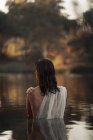 Visão traseira de viajante feminino irreconhecível em tecido refletindo em água pura do lago contra árvores durante a viagem — Fotografia de Stock