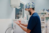 Побочный обзор неузнаваемого врача-мужчины в респираторной маске и однородной дезинфекции рук в больнице — стоковое фото