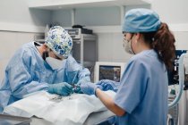 Невпізнаваний чоловічий ветеринарний хірург, операційний пацієнт тварин з медичними інструментами біля помічника жінки в уніформі в лікарні — стокове фото