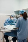 Unrecognizable male vet surgeon operating animal patient with medical tools near female assistant in uniform in hospital — Stock Photo