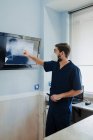 Anonymous male vet in respiratory mask and uniform explaining anatomy of mammal animal while touching screen with X ray illustration in clinic — Stock Photo