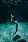 Vista lateral de delgada hembra en traje de baño y aletas nadando bajo el agua en mar turquesa - foto de stock