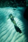 Von oben eine schlanke Frau in Badeanzug und Schwimmflossen, die unter Wasser im türkisfarbenen Meer schwimmt — Stockfoto