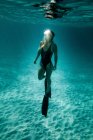 Schlanke Frau in Badeanzug und Schwimmflossen schwimmt unter Wasser im türkisfarbenen Meer — Stockfoto