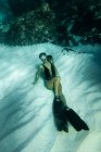 Von oben eine schlanke Frau in Badeanzug und Schwimmflossen, die unter Wasser im türkisfarbenen Meer schwimmt — Stockfoto