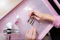 Top view crop esteticista femenina anónima con pinzas que recogen pestañas artificiales de la caja colocada en la mesa de color rosa en el moderno estudio de belleza - foto de stock