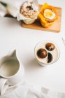 Верхний вид композиции сладких шоколадных бомб, тающих в стакане свежего горячего молока, размещенных на столе рядом вкусные кексы и молочный кувшин — стоковое фото