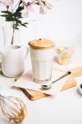 Cucharadita con espuma batida dulce sobre un delicioso café con leche fresco servido en la tabla de cortar de madera en la cocina moderna de luz - foto de stock