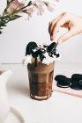 Crop anonymous person decorating sweet yummy frappe drink with chocolate cookies on whipped cream in light kitchen — Stock Photo