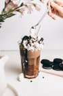 Ernte anonyme Person dekoriert süßen leckeren Frappé-Drink mit Schokoladenkeksen auf Schlagsahne in heller Küche — Stockfoto