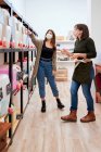 Full length of female customer in mask choosing eco friendly detergent while consulting with seller in shop — Stock Photo
