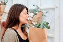 Vista lateral do cliente feminino da florista loja cheirando monte de flores envolto em pacote de papel com os olhos fechados — Fotografia de Stock